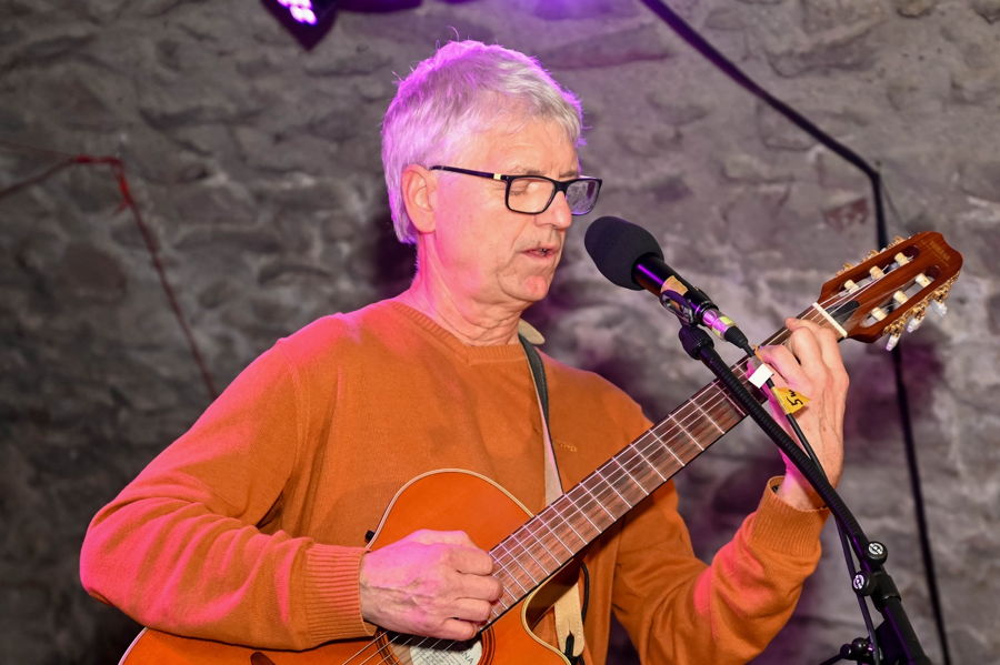 Älterer Mann singt und spielt Gitarre am Mikrofon auf einer Bühne